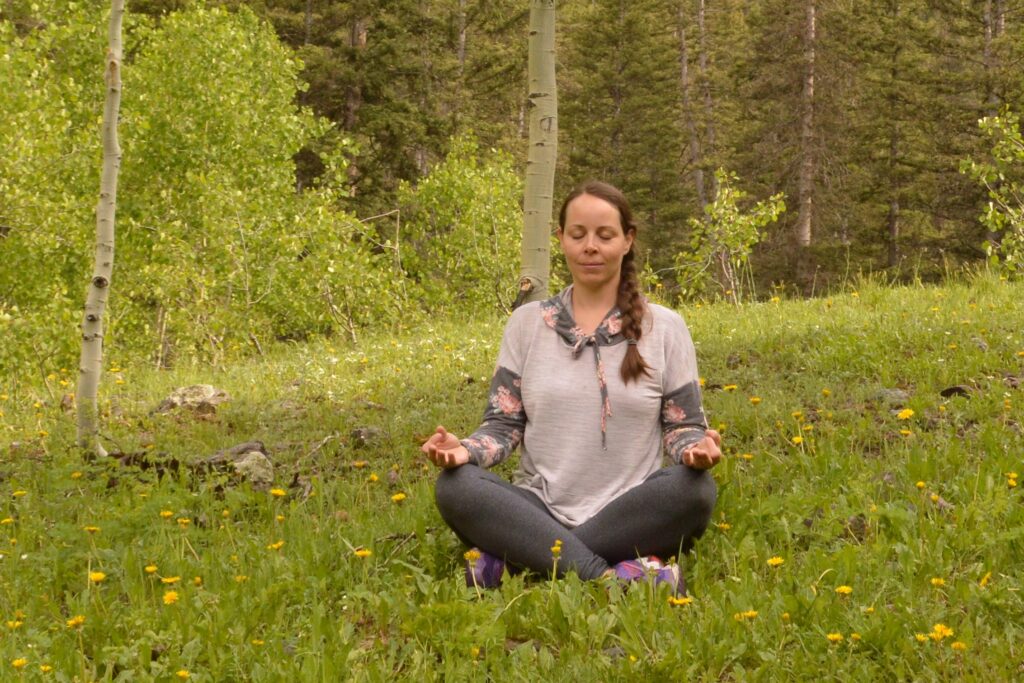 Christina sitting cross-legged in a forest practicing breath awareness