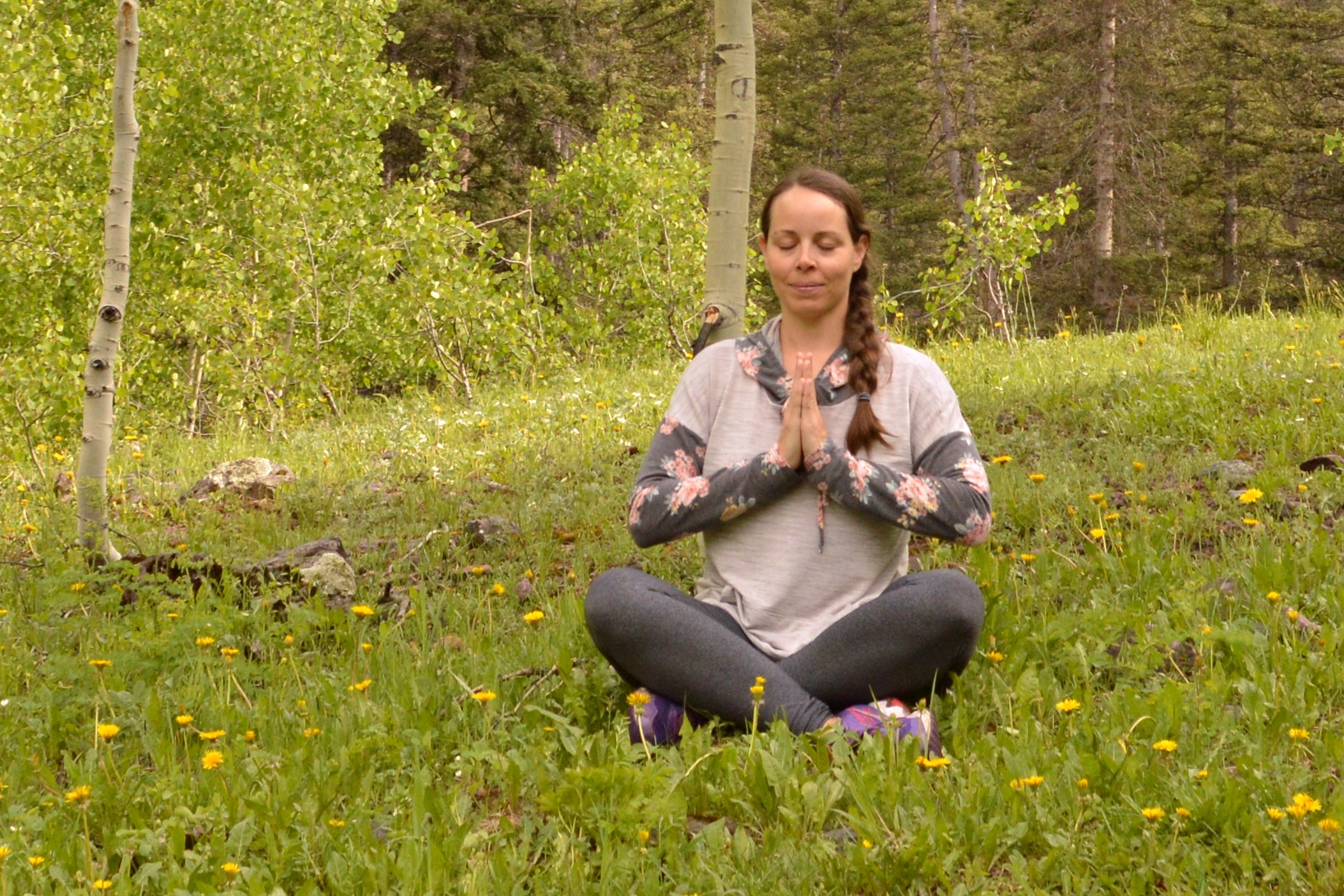 Christina sitting in a forest with eyes closed practicing faith-based yoga