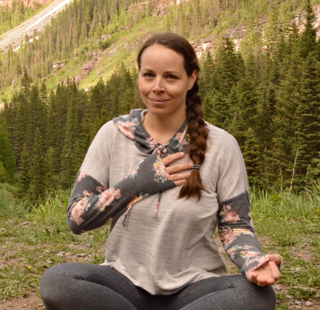 Christina seated in an alpine setting with her hand on her heart
