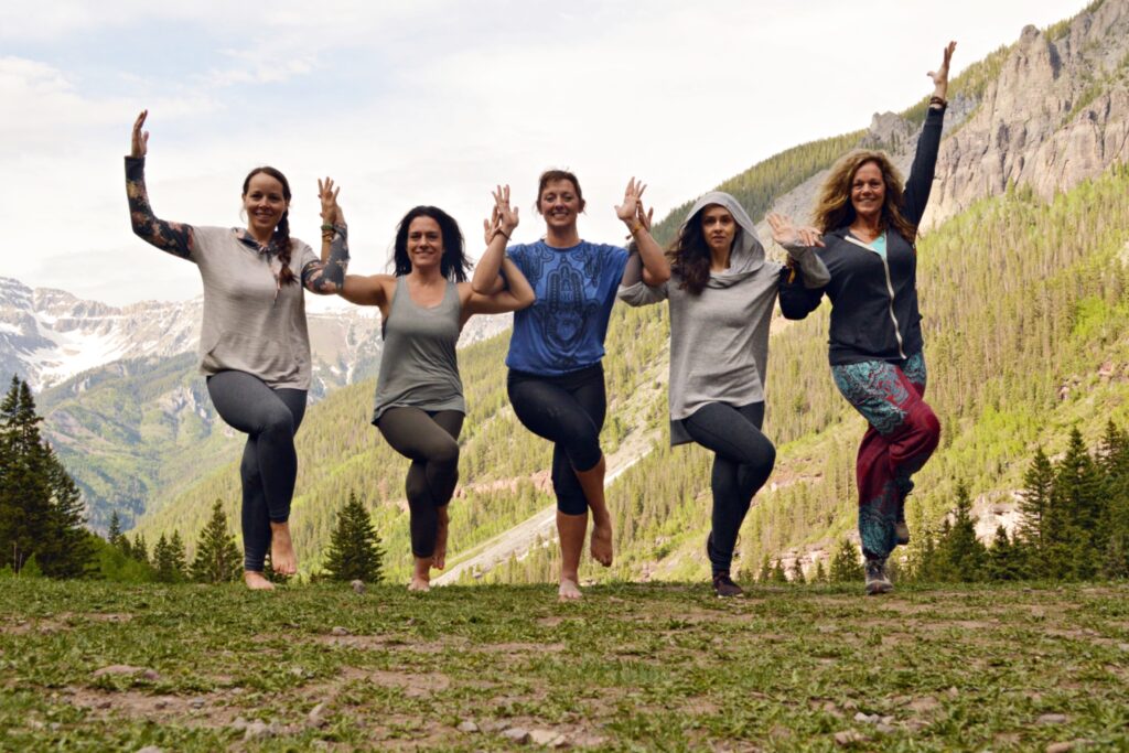 A group of yogis in an alpine setting with arms connected in eagle pose